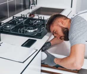 Young professional plumber in grey uniform working on the kitchen.